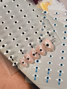 Macro shot of evil eye nail stickers with black and blue designs on nude pink nails