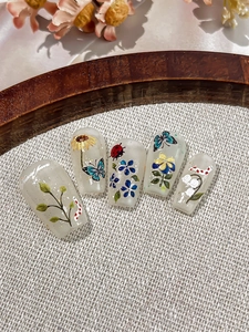 Detailed macro view of handmade nail tips with sunflowers, butterflies and nature patterns