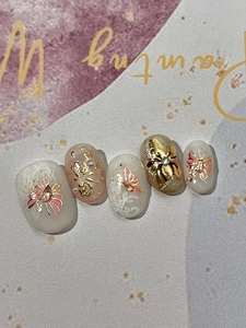 Detailed view of handmade press-on nails with golden butterfly relief and pearls