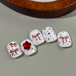 Polka dot press-on nails with red bows and 3D floral gemstone on a grey background