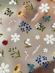 Macro detail of 3D embossed nail art stickers featuring sunflowers, daisies and butterflies