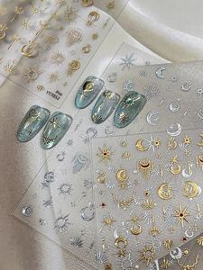Close-up of gold celestial nail stickers with sun moon and star patterns on blue nails