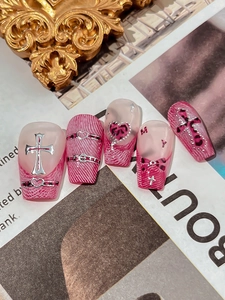Detail view of pink and white coffin nails with silver crosses and leopard pattern