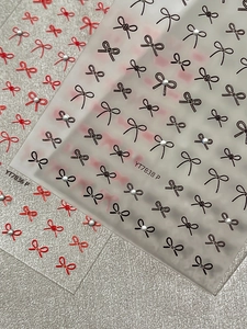 Detailed bow nail art stickers in red and black with white pearls on silver texture