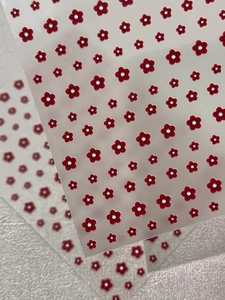 Macro detail of 5-petal red flower embossed nail art stickers on a textured white fabric