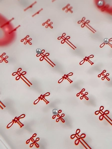 Macro view of red Chinese knot nail art stickers with small silver pearls on white background