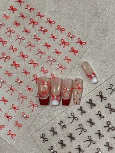 Close-up of 3D red and brown bow nail stickers with pearls on a textured background