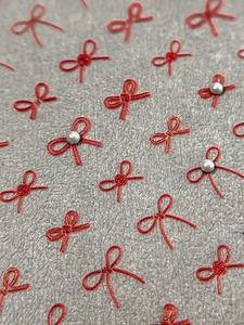 Detailed macro view of 3D red bow nail stickers with pearl accents on grey texture
