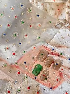 Detail of metallic gold star and sunburst nail stickers with colorful crystal accents