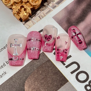 Pink leopard print press-on nails with silver cross and heart charms in Y2K style