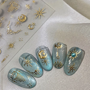 Golden celestial nail stickers with moon and star designs on dark blue cat-eye nails