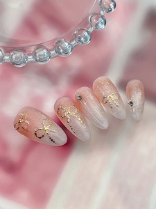 Detail of almond nails with pink cat-eye gradient, gold bows and sparkling rhinestones