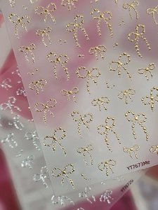 Close-up of 3D metallic bow nail art stickers in gold and silver finish with embossed texture
