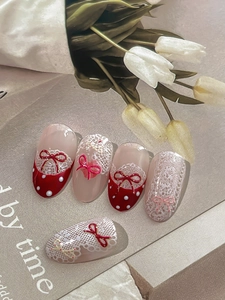 Detailed view of red press-on nails with 3D bows, white polka dots and lace patterns