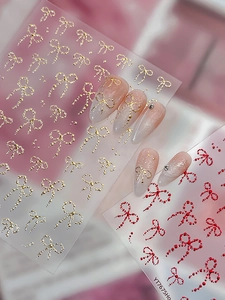 Detail of bow-shaped nail stickers with gold relief and red dots on almond nails