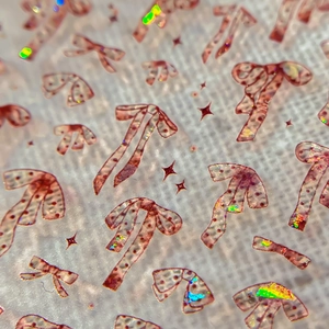 Pink laser nail stickers with sparkling bow and star patterns on textured white fabric