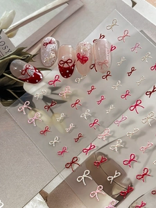 Close-up of embossed bow and polka dot nail art stickers in pink and red tones