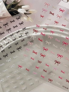 Detailed view of 3D embossed bow nail stickers in various colors on a white plate