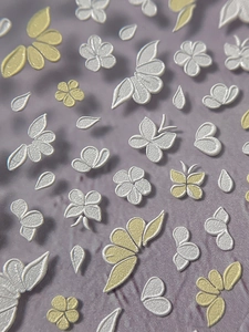 Macro shot of 5D embossed floral nail stickers featuring white butterflies and gold flowers