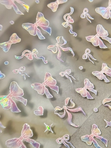 Close-up of holographic 3D bow and heart nail art stickers with laser rainbow finish