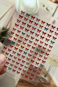Macro shot of 3D embossed nail art stickers with red and blue bow designs and gold edges