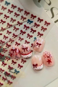 Macro shot of 3D retro bow nail stickers in red and blue on pink false nails