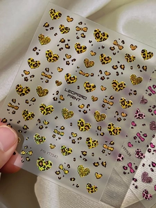 Close-up of leopard print heart and bow nail decals on translucent backing sheet