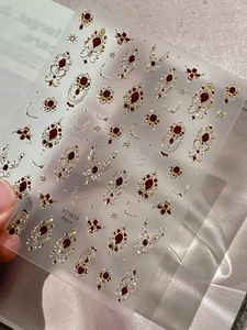 Macro shot of Baroque gold foil nail stickers with red faux gems and ornate patterns
