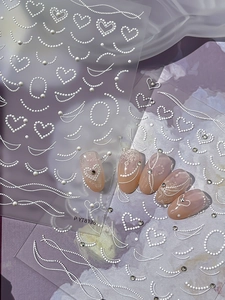 Detail of 3D white pearl nail stickers with heart patterns on pink nails