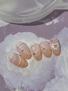 Detail of pink almond nails with lace pattern, tiny pearls, and heart-shaped rhinestones