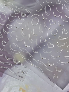 Detailed macro view of 3D pearl heart and curved line nail art stickers on purple cloth