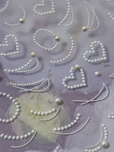 Macro detail of 3D embossed heart and pearl chain nail art stickers on pastel backdrop