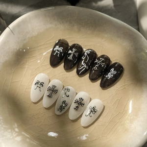 Detail of gothic press-on nails featuring 3D silver crosses and bow art on a ceramic dish