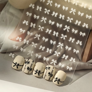 Self-adhesive white bow nail stickers with rhinestone accents on almond-shaped nails