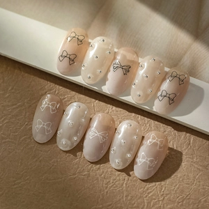 Detail of pink bow press-on nails with pearl finish and silver bead embellishments