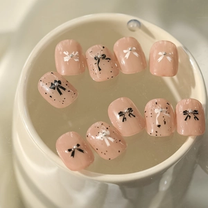 Detail view of 10-piece nude pink press-on nails with black bows and polka dots decoration