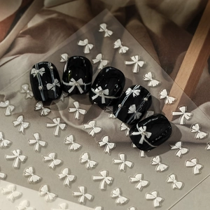 Close-up of black glossy press-on nails with white bows and sparkling silver rhinestones