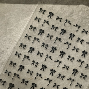Detailed view of high-quality 3D black bow nail art stickers on transparent backing sheet