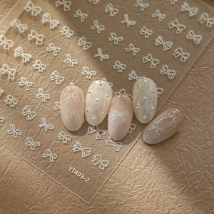 Macro detail of white bow nail stickers YT493-2 with silver pearl accents on nude nails