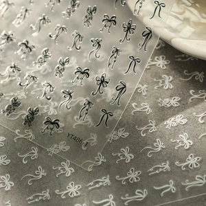 Close-up of minimalist black and white bow nail art stickers with fine embossed details
