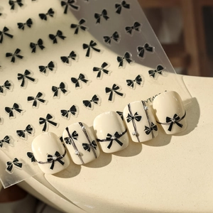 Close-up of black bow nail stickers with rhinestone accents on creamy white base nails