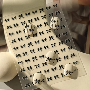 Close-up of black and white bow nail stickers applied on cream-colored fake nails