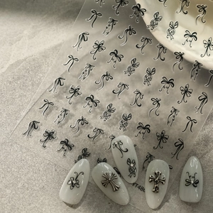 Detail of black ribbon bow nail art stickers applied on white manicure with silver crosses