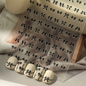 Detail of black bow nail art stickers with 3D rhinestones on glossy beige nails