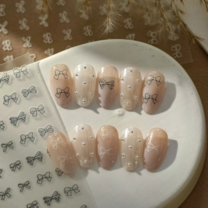 Detail of pink gradient press-on nails with silver pearls and bow tie sticker patterns
