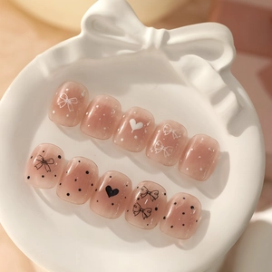 Gros plan d'un kit de nail art rose avec des motifs de nœuds, cœurs et pois sur ongles ronds