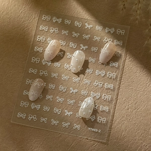Detail of white bow nail stickers and silver bead accents on manicured nails