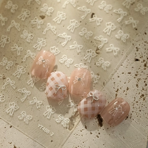 Detailed pink nail stickers with 3D metal bows and grid patterns on stone surface