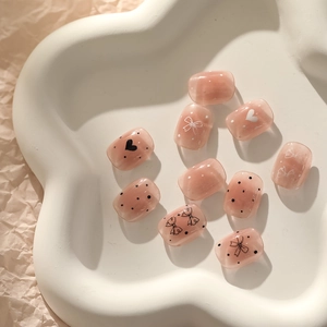 Détail de faux ongles gel rose avec motifs nœuds et cœurs sur plateau en céramique