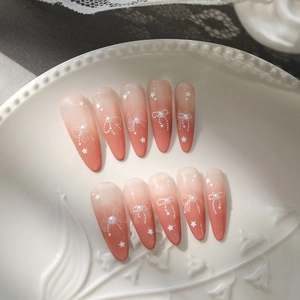 Detailed view of pink ombre press-on nails with 5D embossed bows and pearls on a ceramic plate